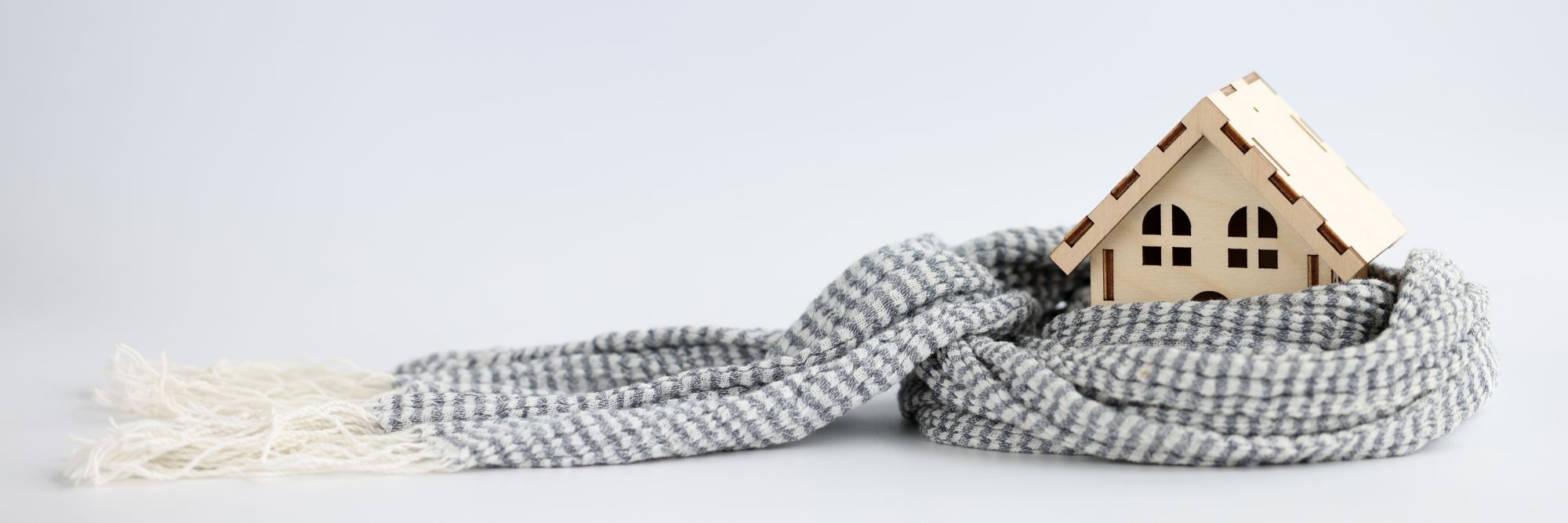 Small wooden house wrapped in scarf on white background closeup
